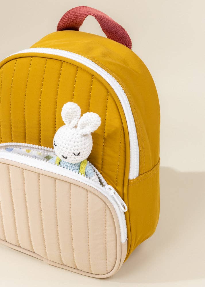 Yellow backpack with a plush toy attached to the zipper on a beige background