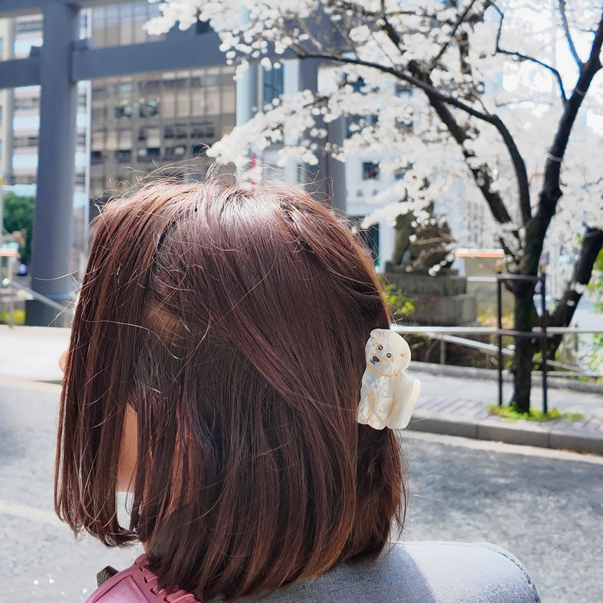 Person with a short haircut standing in front of cherry blossom trees