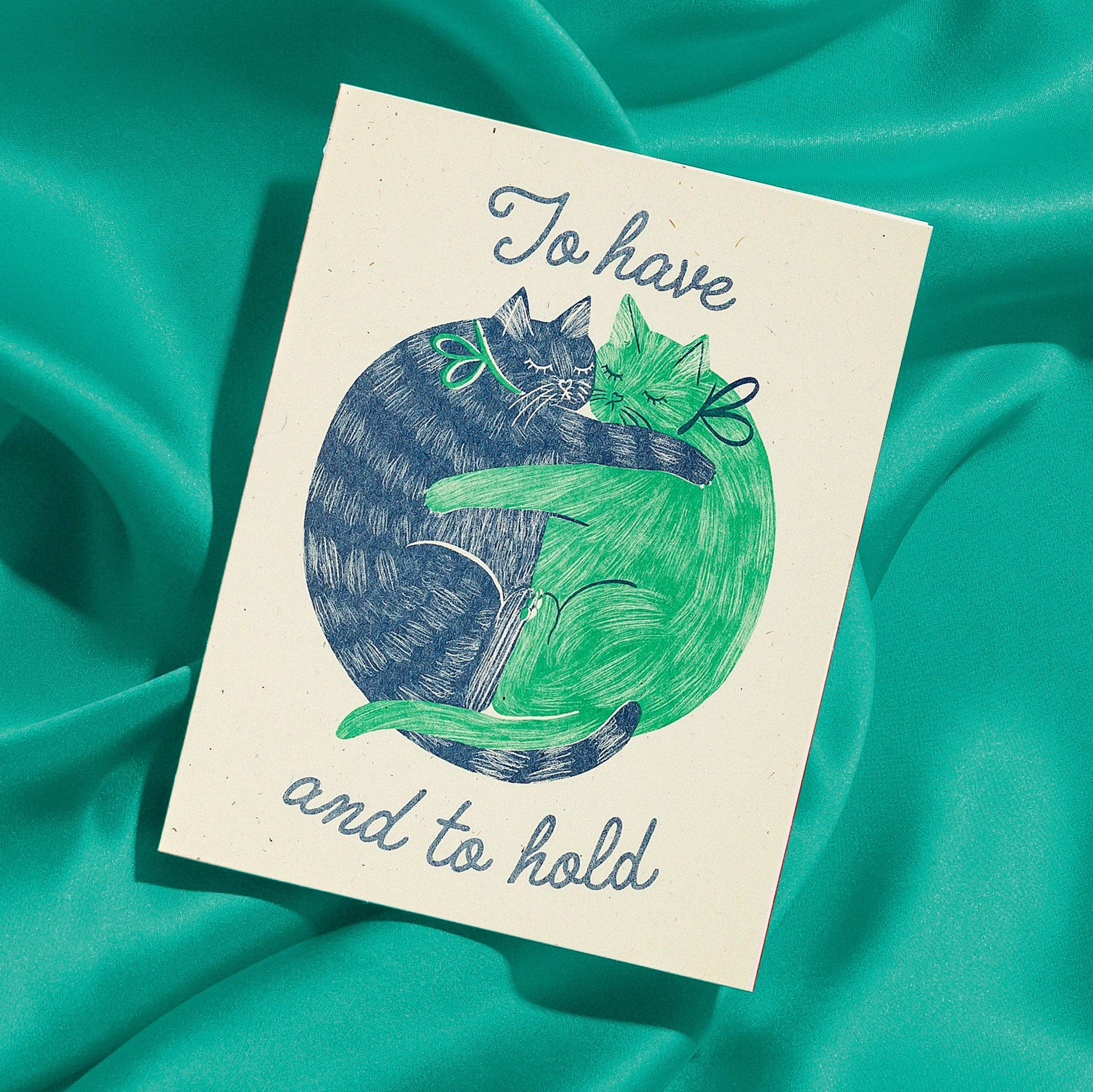 Card with a blue and green cat illustration and text on a teal fabric background