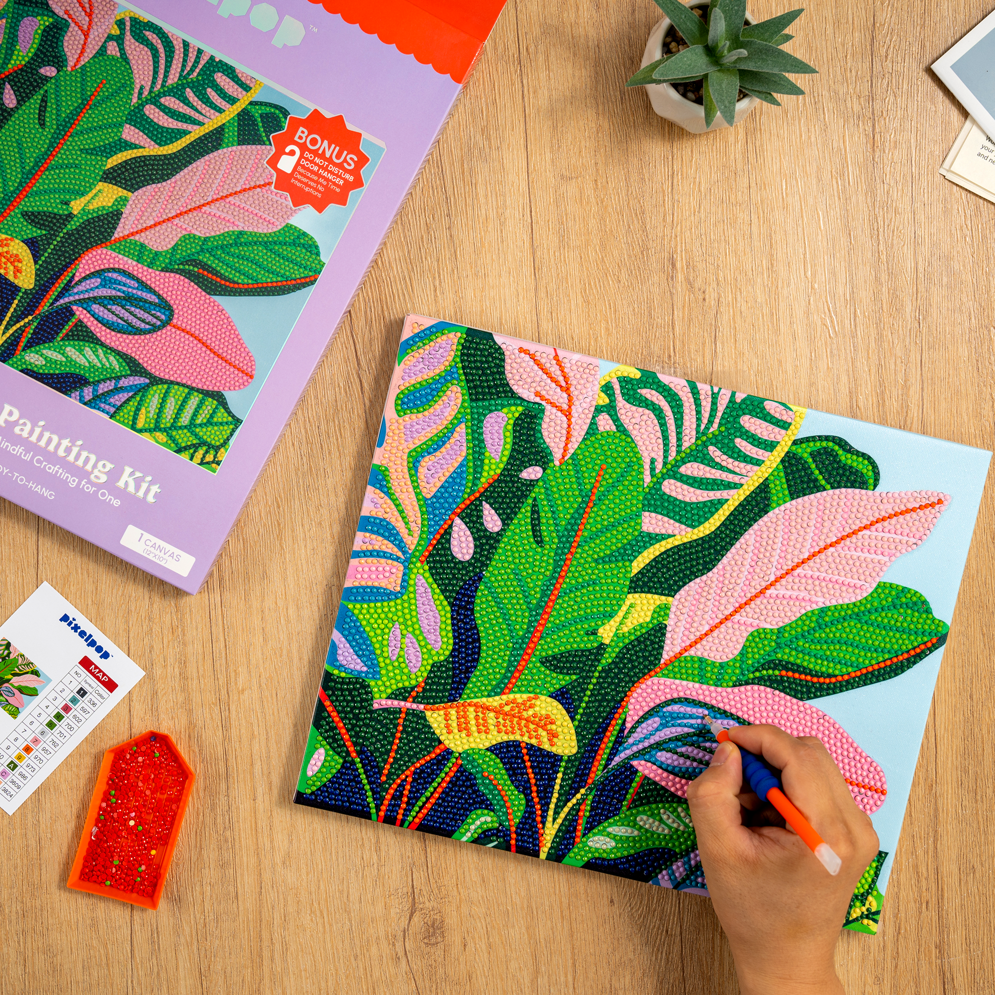 Colorful leaf-patterned painting kit being used on a wooden surface with a hand holding a paintbrush.