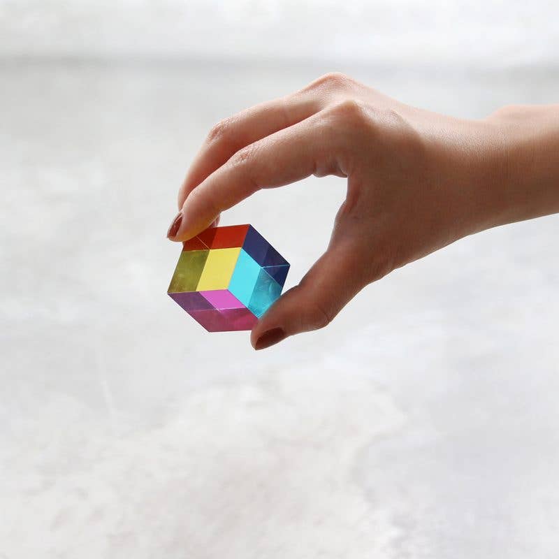 Hand holding a small, colorful 3D puzzle cube against a light background