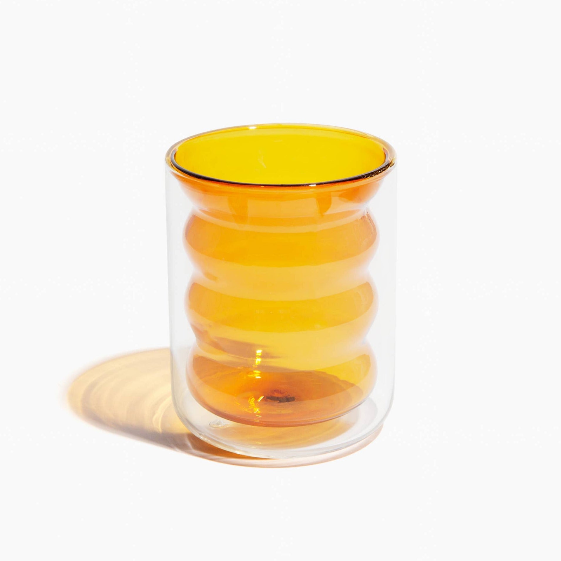 Clear glass tumbler with yellow interior and rim on a white background