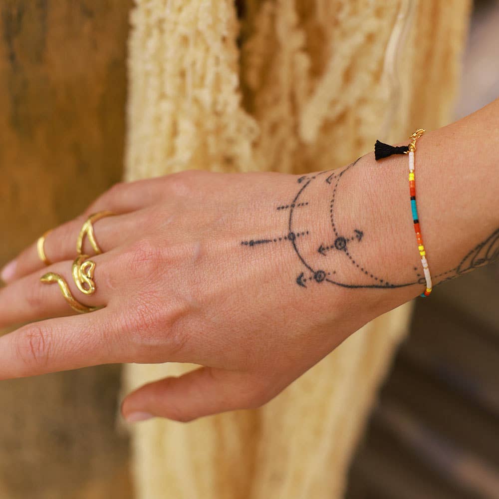 Hand with tattoos, gold rings, and a colorful bracelet against a blurred background