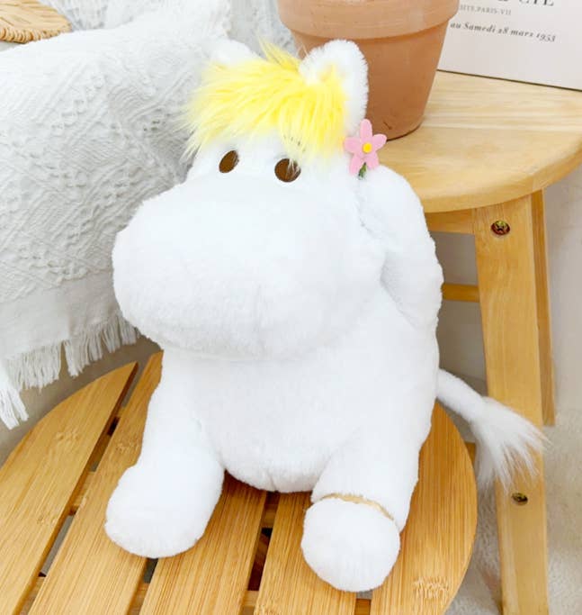White plush toy with yellow hair and a pink flower on a wooden surface