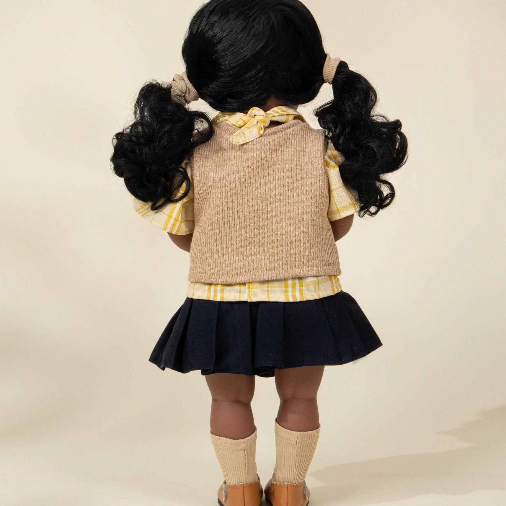 Doll wearing a school uniform with a beige vest and black skirt on a beige background
