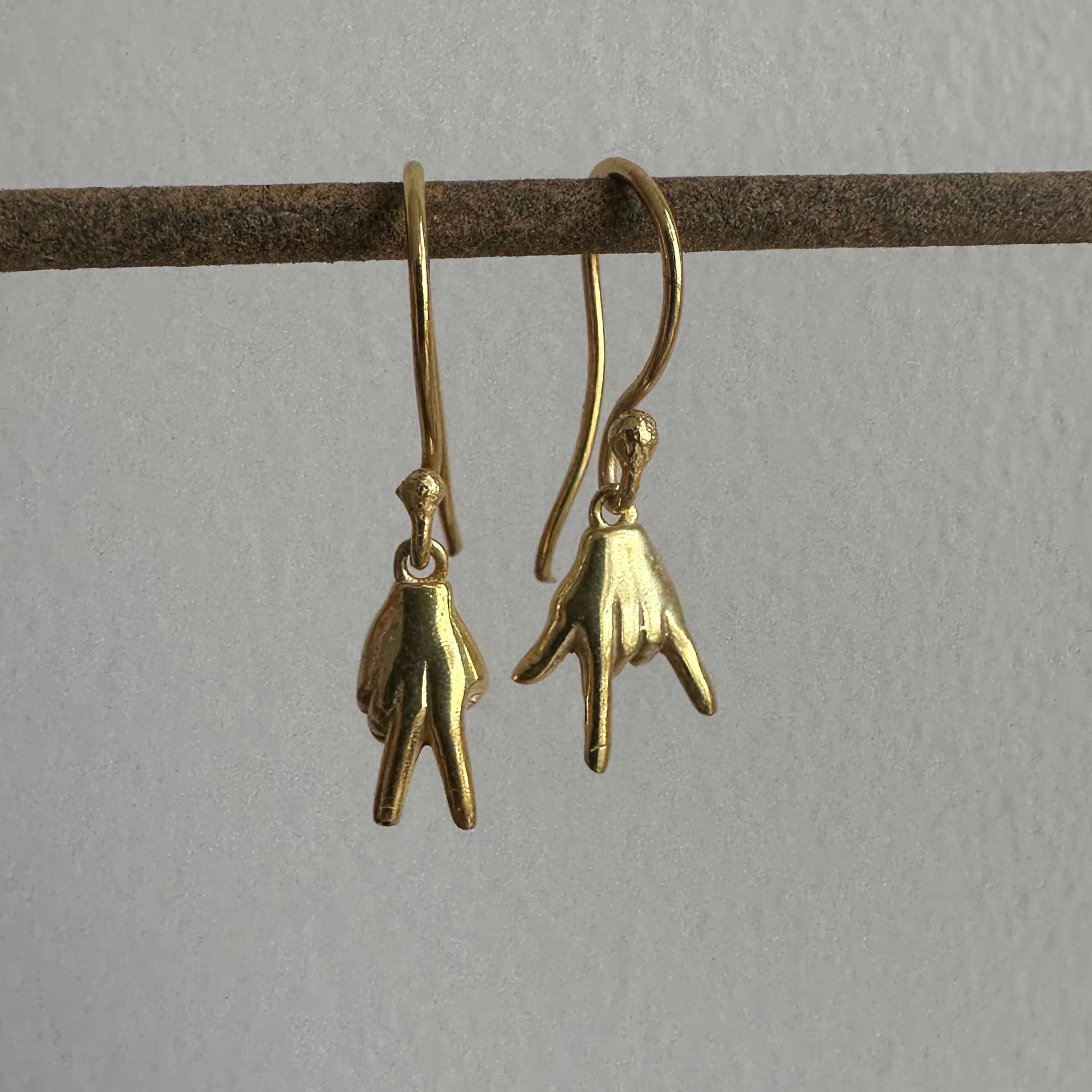 Gold hand-shaped earrings on a thin brown rod against a light gray background