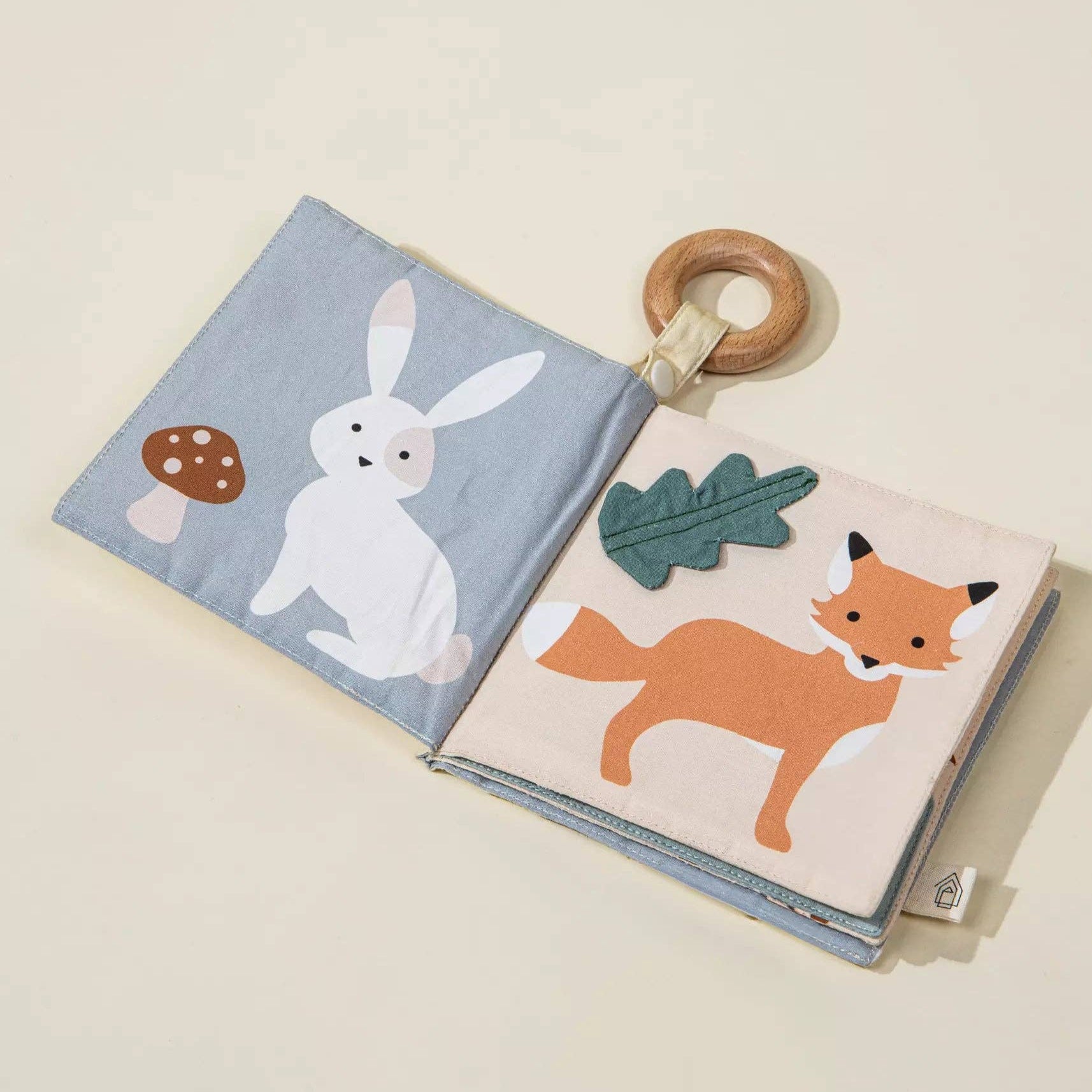 Children's soft book with animal illustrations and a wooden ring on a beige background