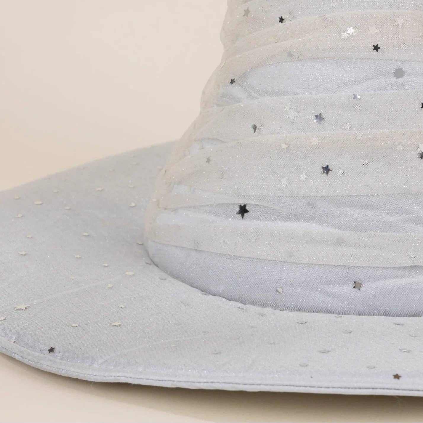 A close-up of a light gray fabric hat with horizontal pleated stripes and scattered silver star embellishments, set against a plain beige background.