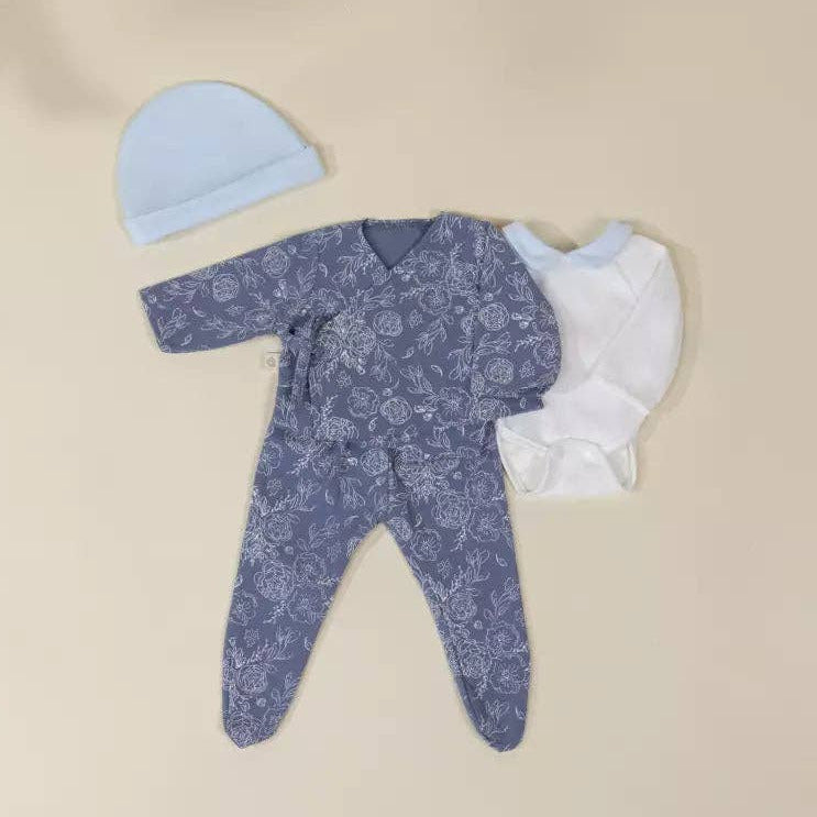Baby outfit set with blue floral onesie, hat, and booties on a beige background