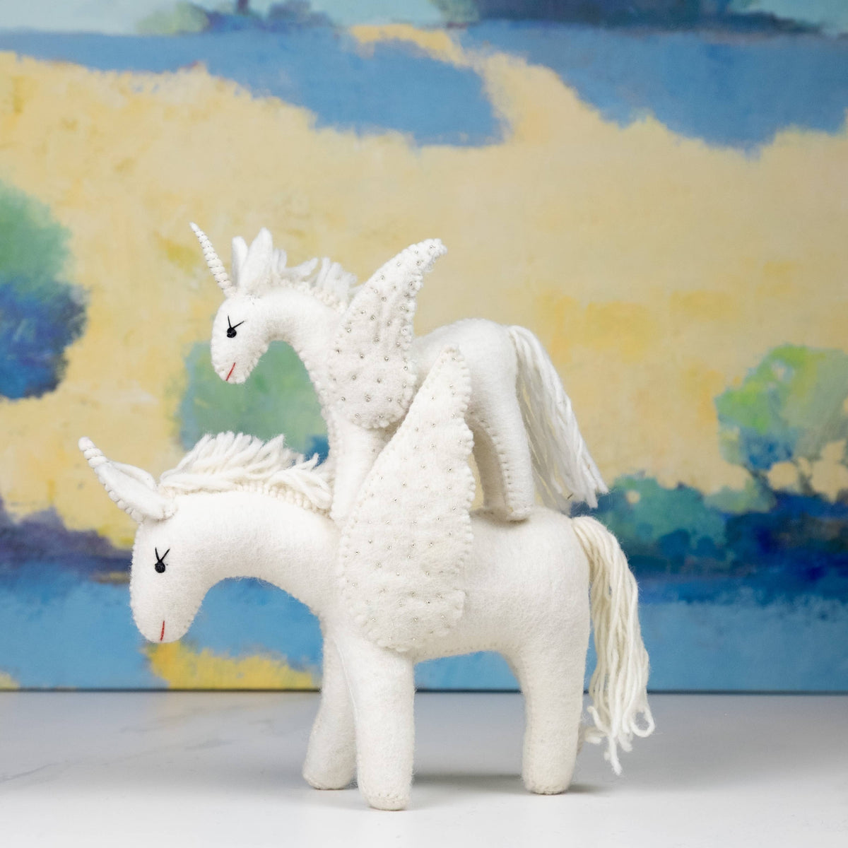 Two white unicorn toys with a colorful abstract background