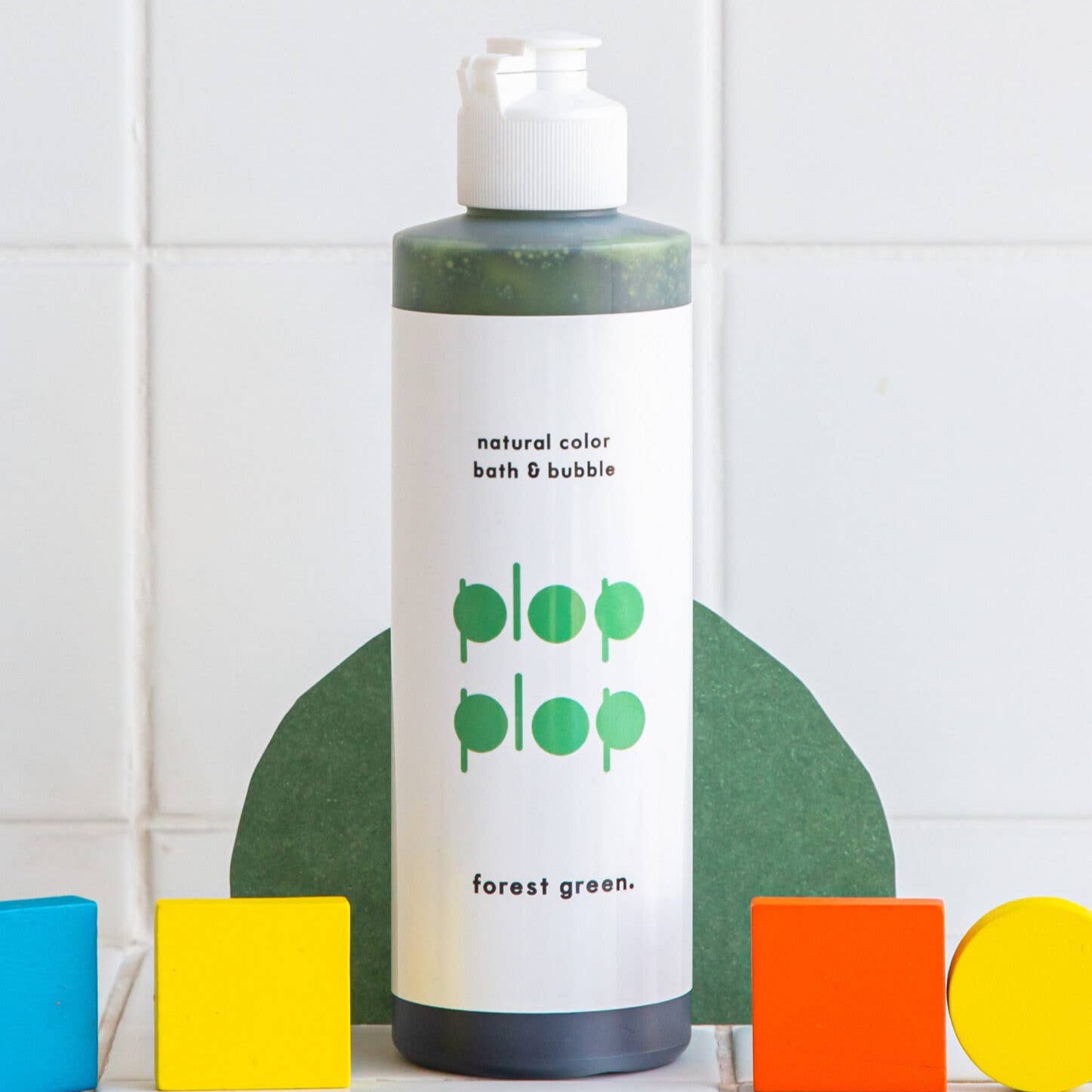 Bottle of 'plop plop' bath and bubble product on a tiled wall background with colorful blocks.