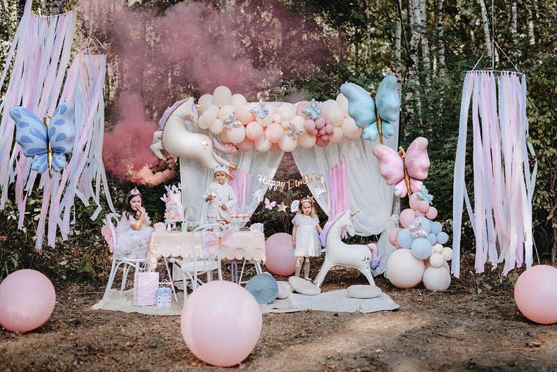 Children's birthday party setup with balloons, decorations, and children in a forest setting.