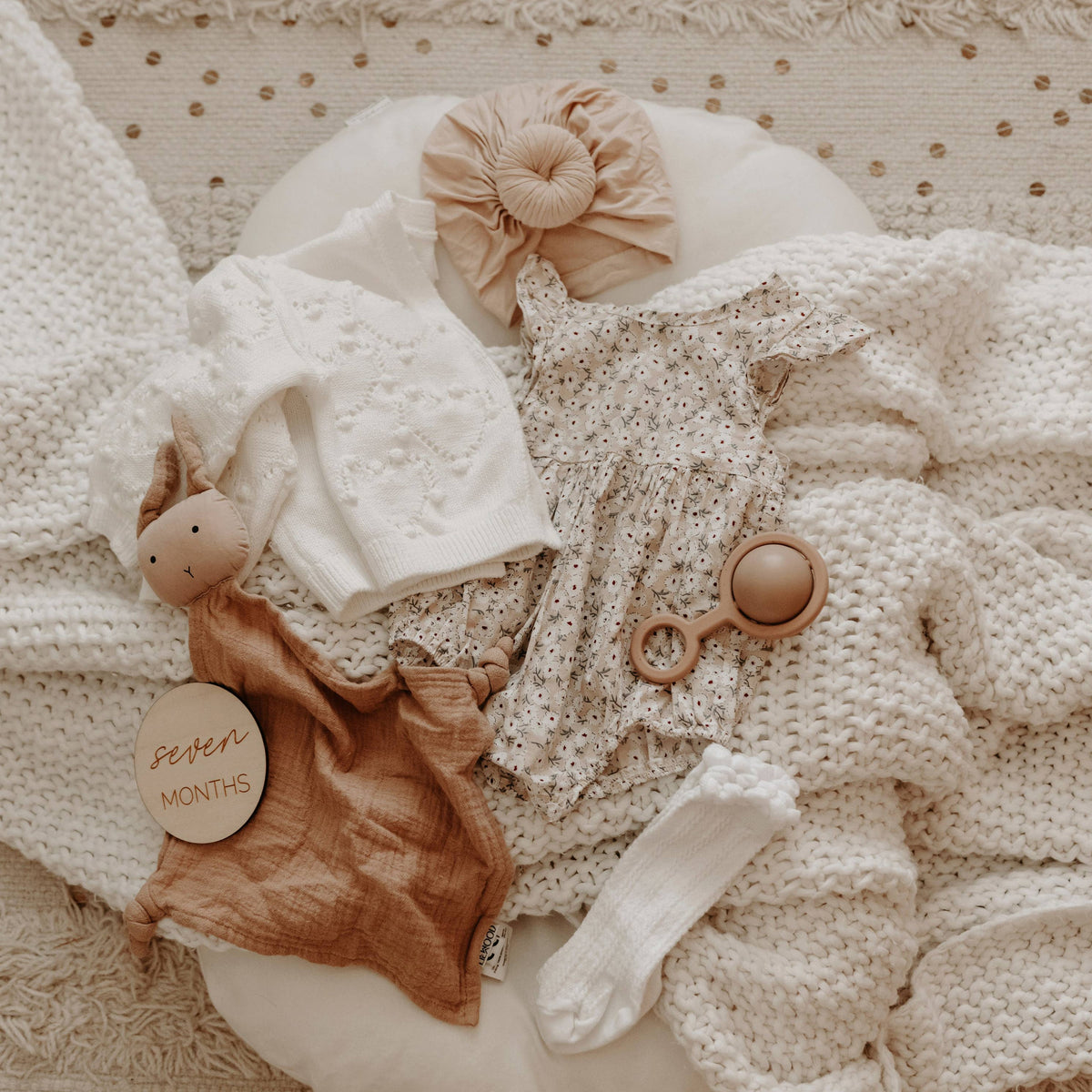 Baby clothing and accessories on a textured beige surface