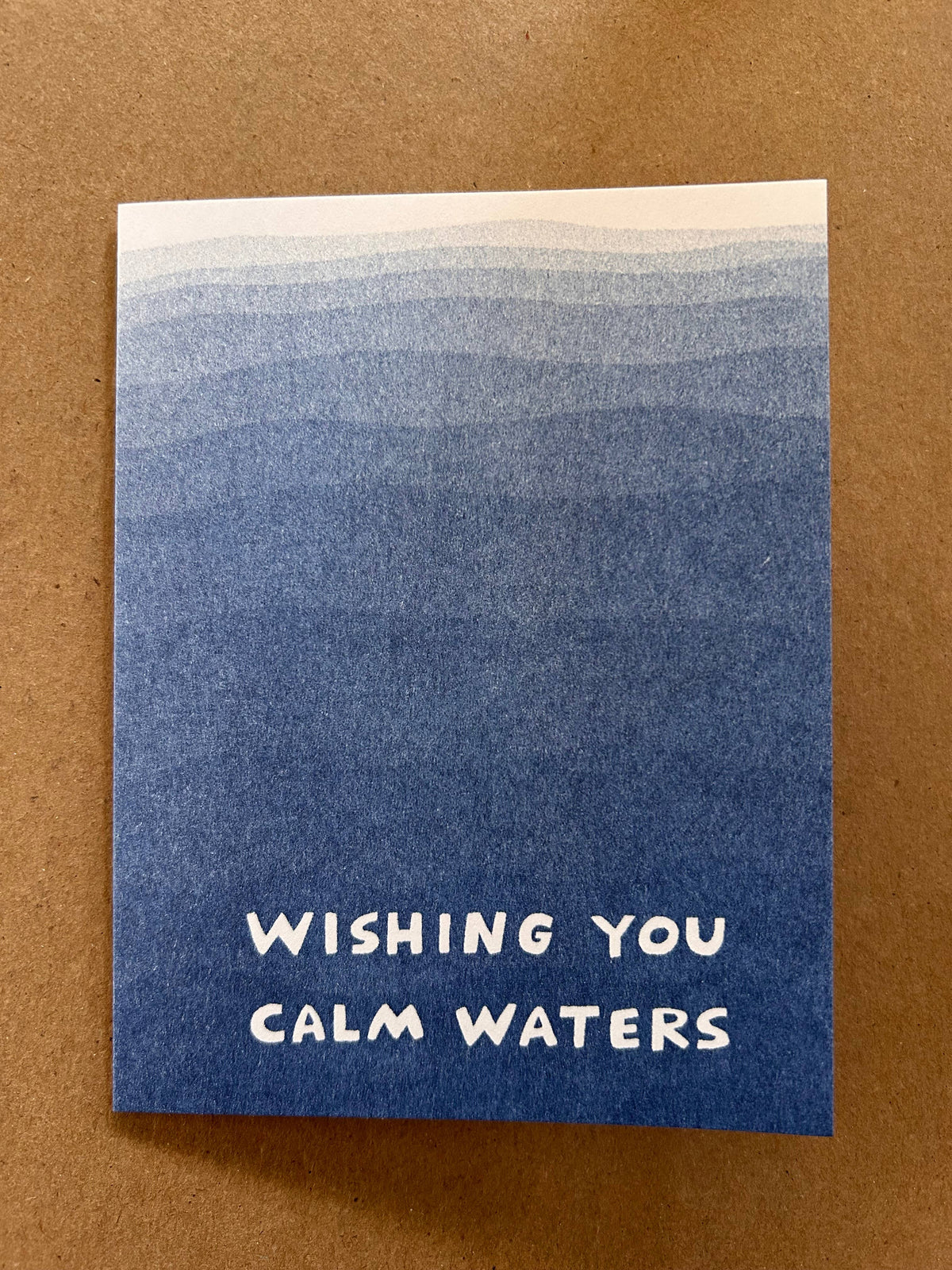 Blue card with 'Wishing you calm waters' text on a brown background