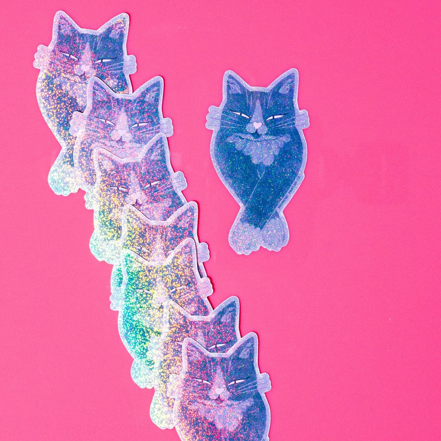 A set of glittery cat-shaped stickers in various pastel colors, including pink, purple, blue, and green, arranged on a solid bright pink background.