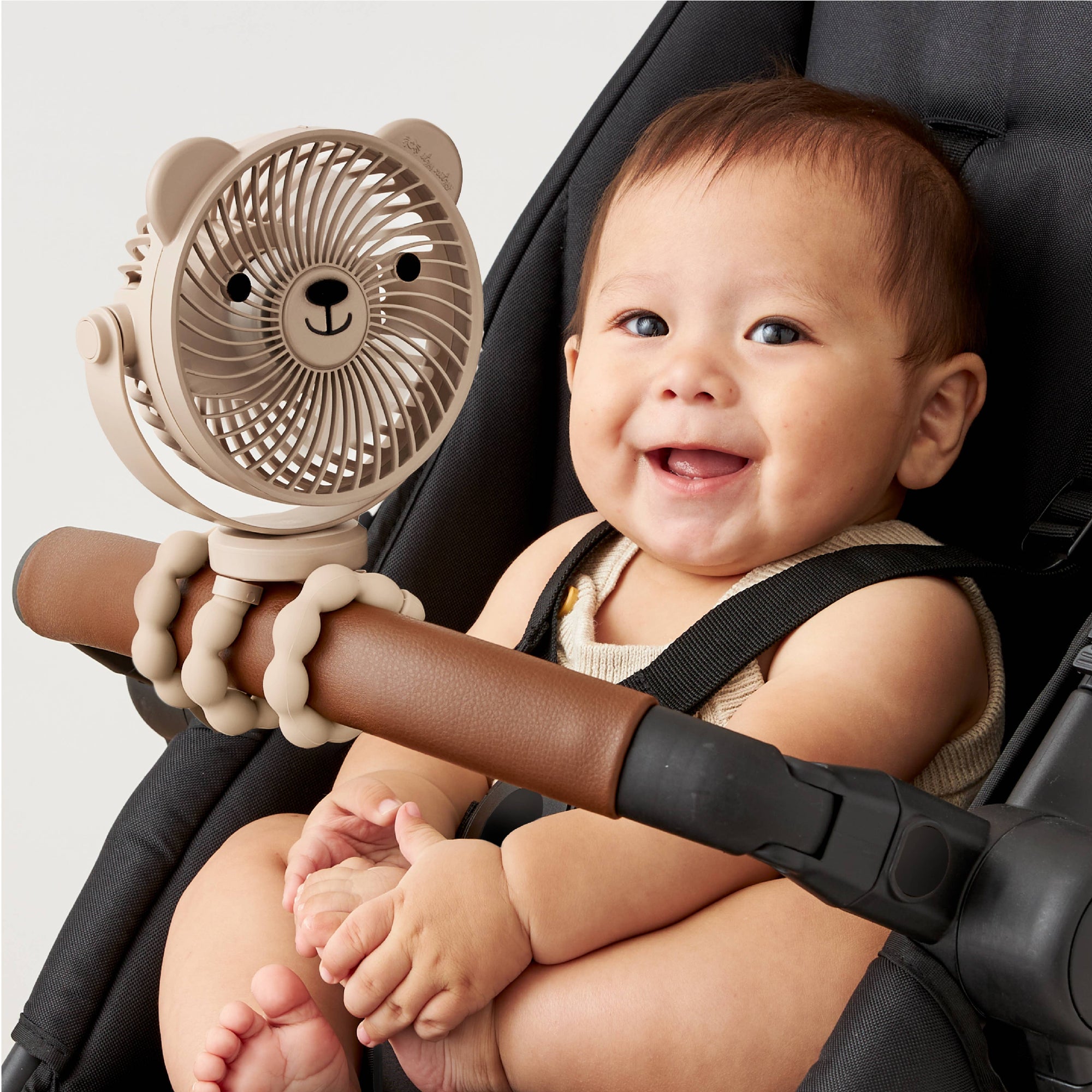 Baby sitting in a stroller holding a bear-shaped fan.