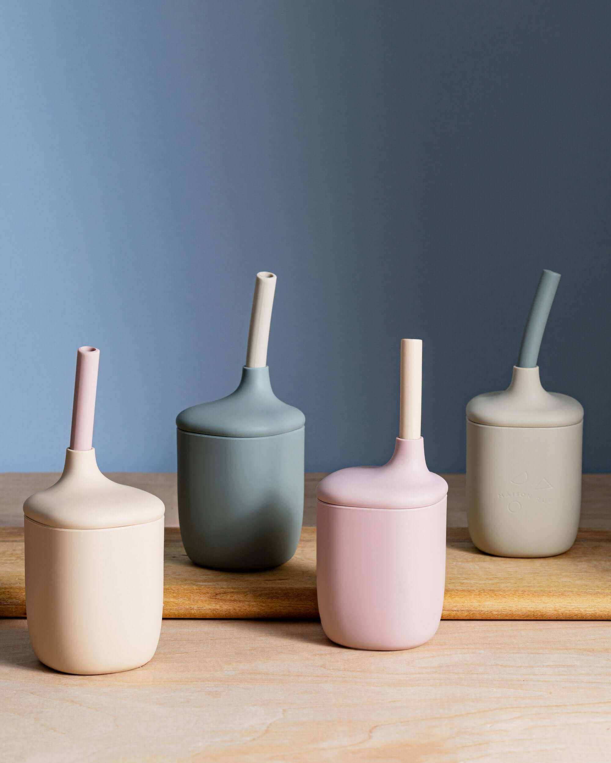 Five silicone cups with straws on a wooden surface against a blue wall