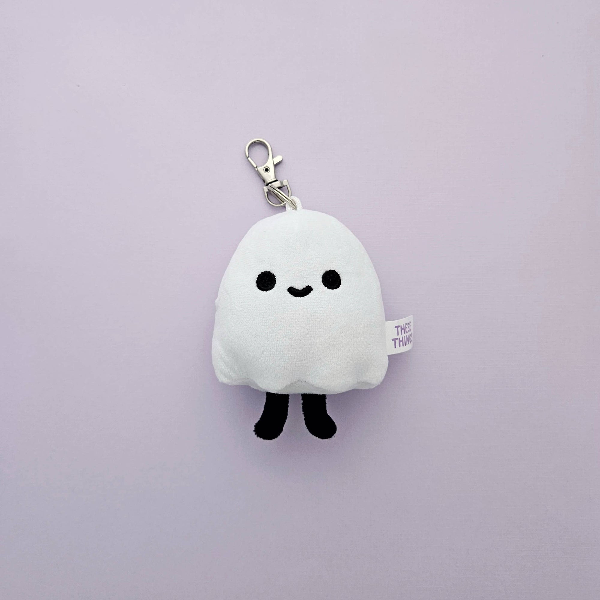 Plush ghost keychain with a smiley face on a light purple background