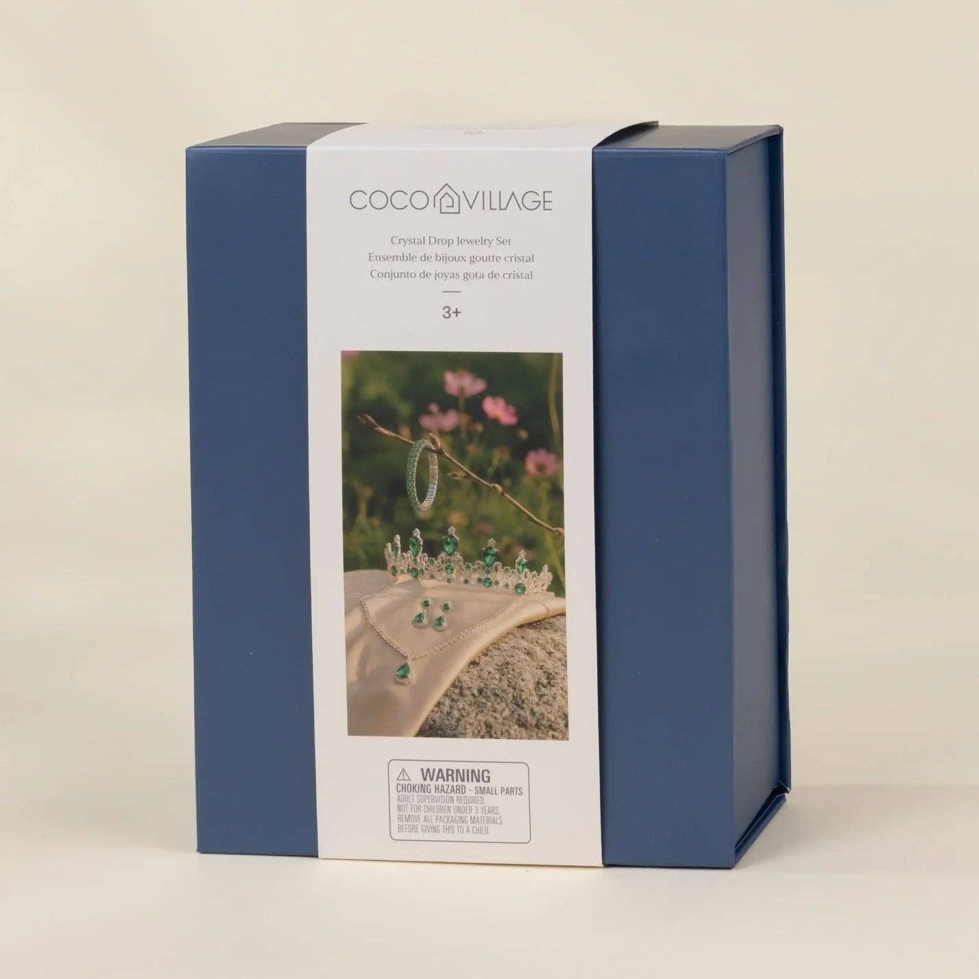 COCO VILLAGE brand product box in navy blue and white packaging, featuring a photo of a tiara on a beach, photographed against a neutral cream background.