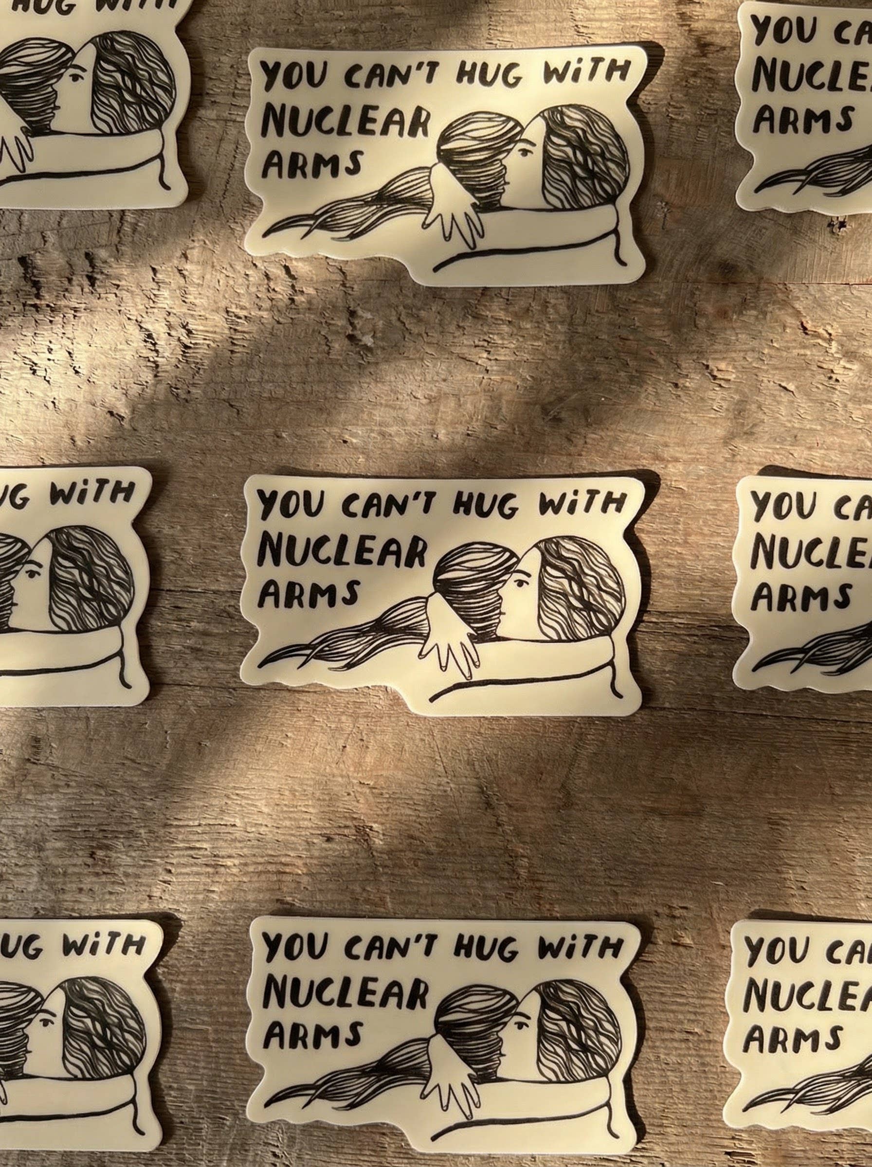 Stickers with illustrations of people hugging and text 'You can't hug with nuclear arms' on a wooden surface.