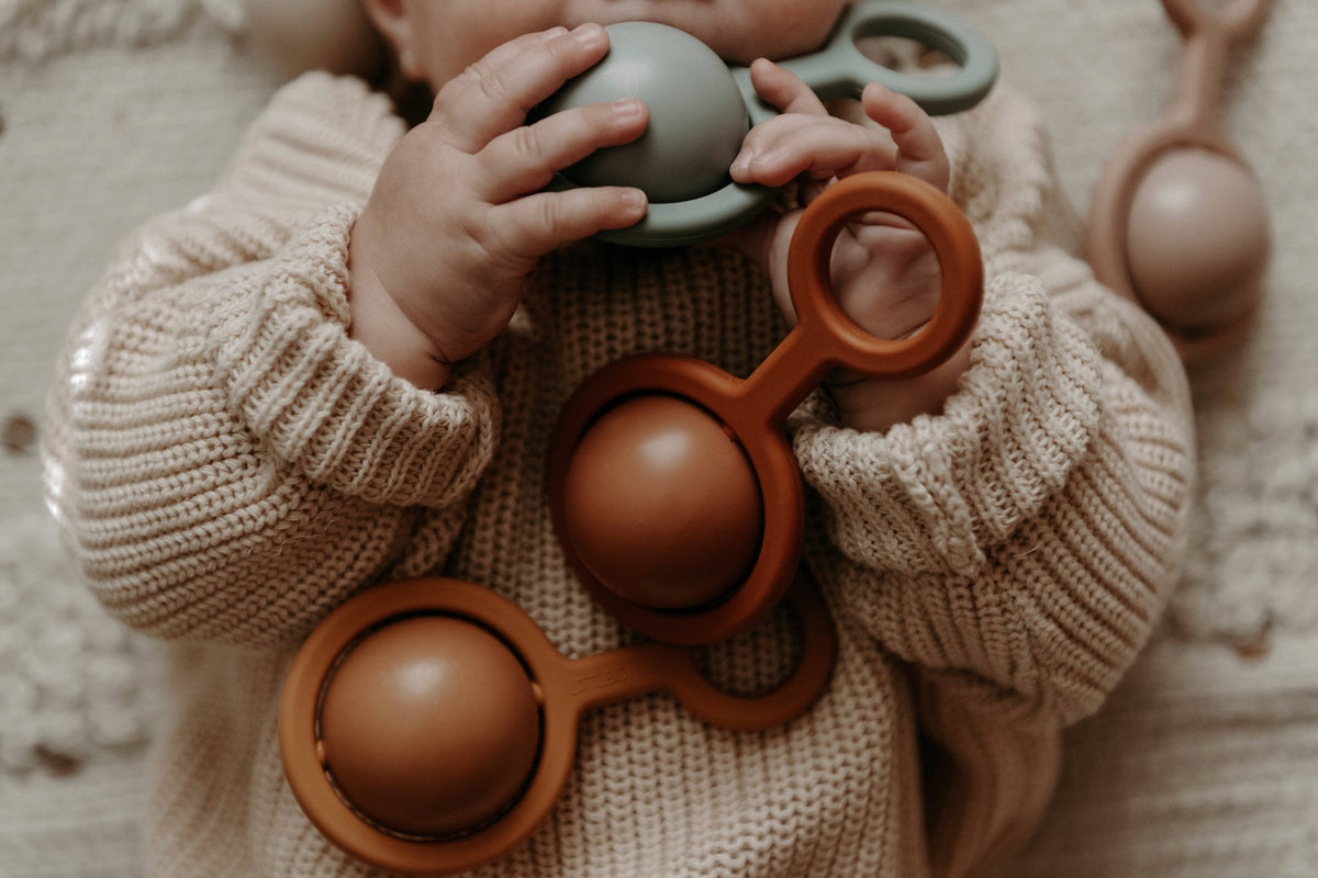 Baby playing with colorful teething toys on a soft surface