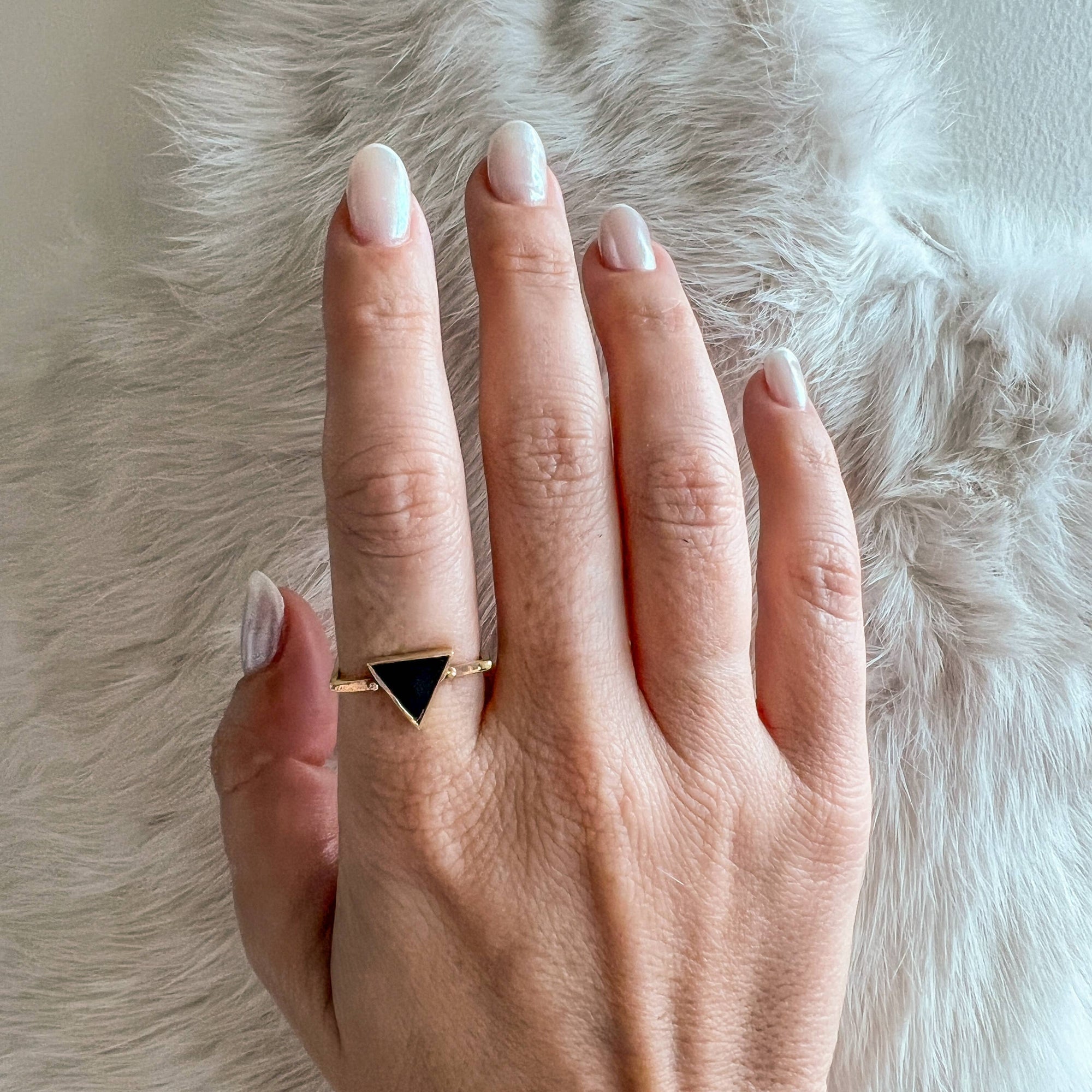 Hand wearing a gold ring with a black triangle on a fluffy white surface