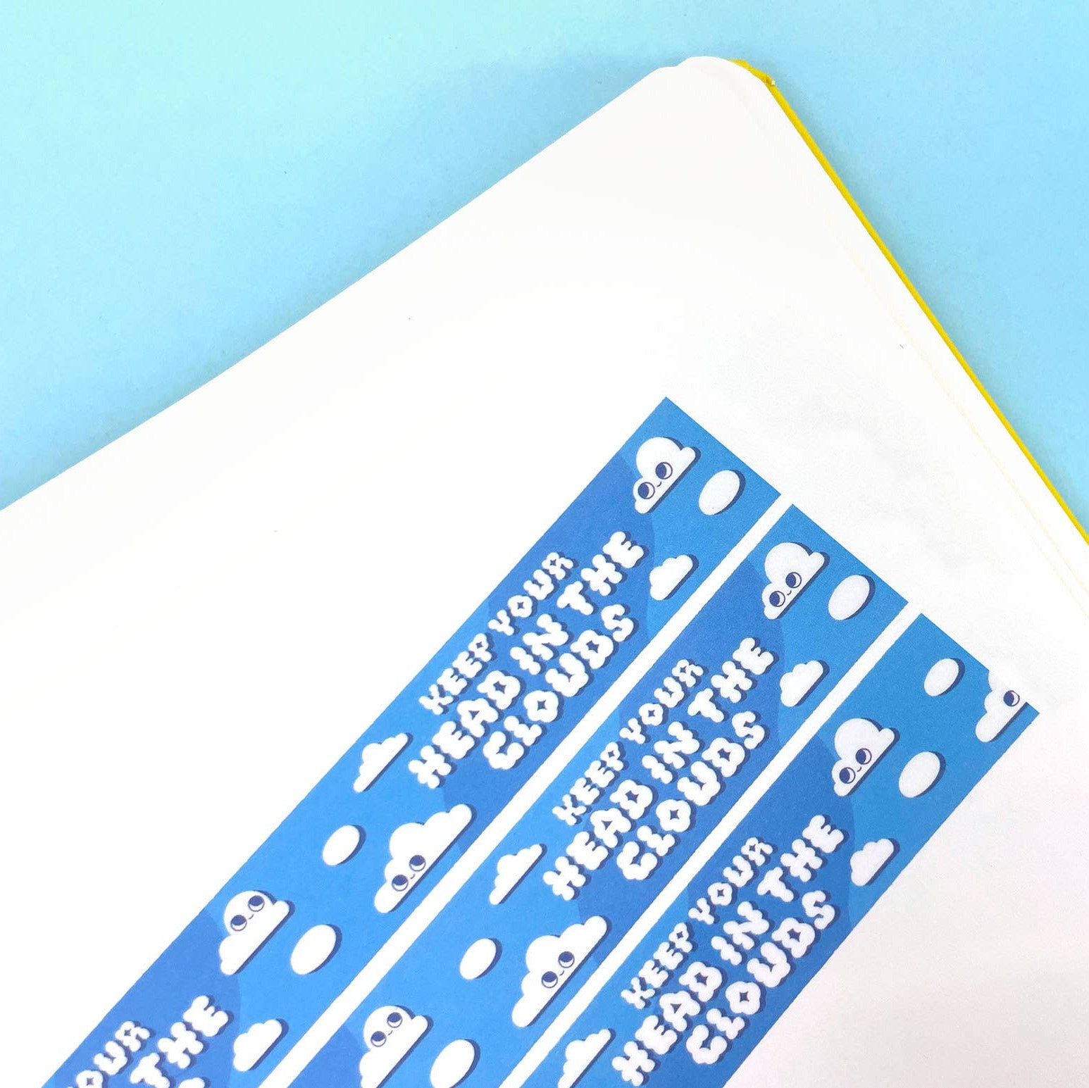 Blue and white sticker with text and cloud designs on a notebook corner against a blue background