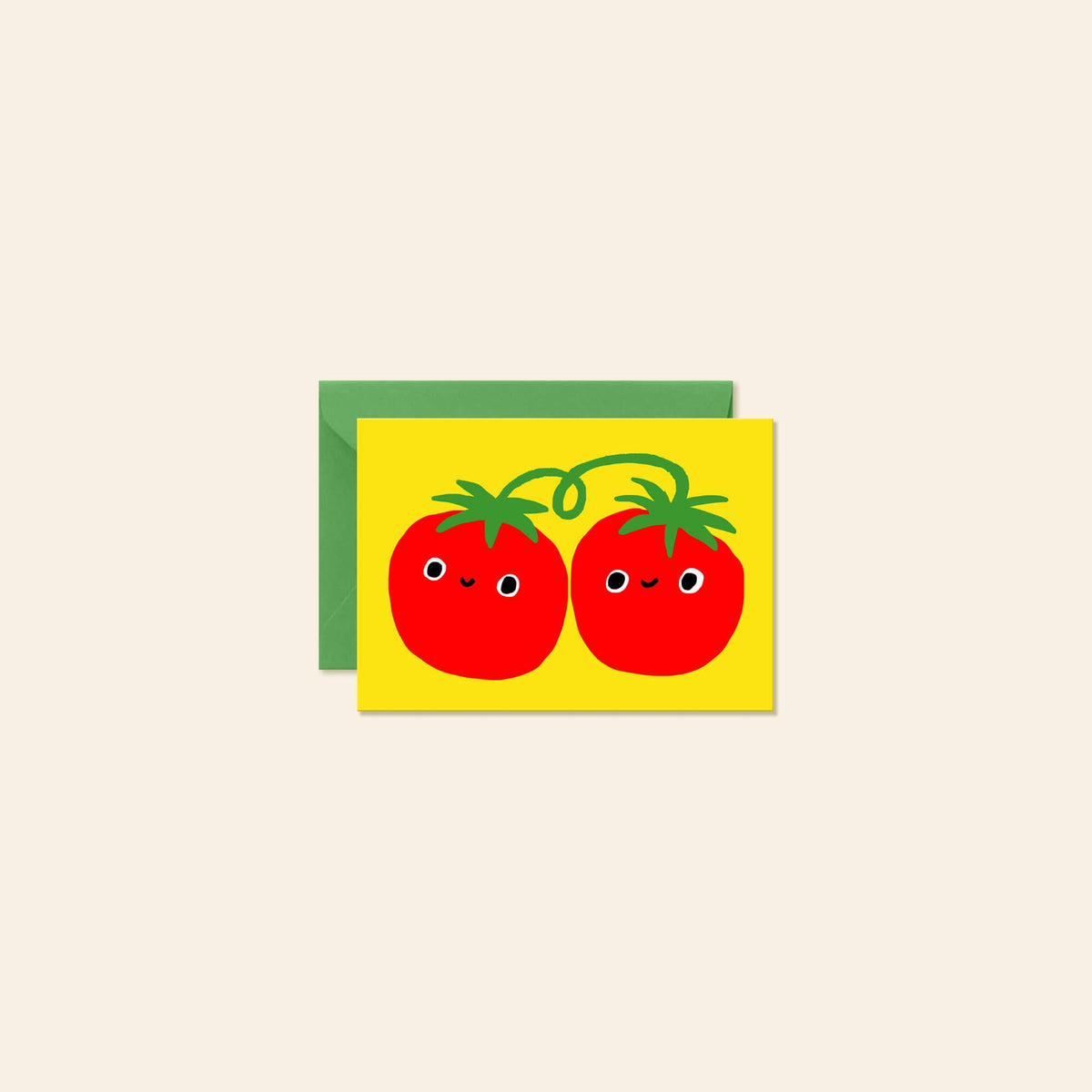 A greeting card with a bright yellow front featuring two cute red cartoon tomatoes with green tops and faces, shown with a green envelope behind it on a light beige background.
