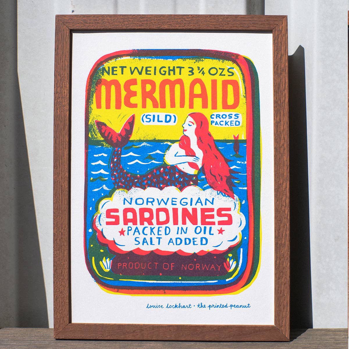 Framed artwork of a vintage sardine can label with a mermaid design.