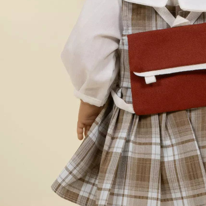 doll wearing a plaid dress with a red bag on a beige background