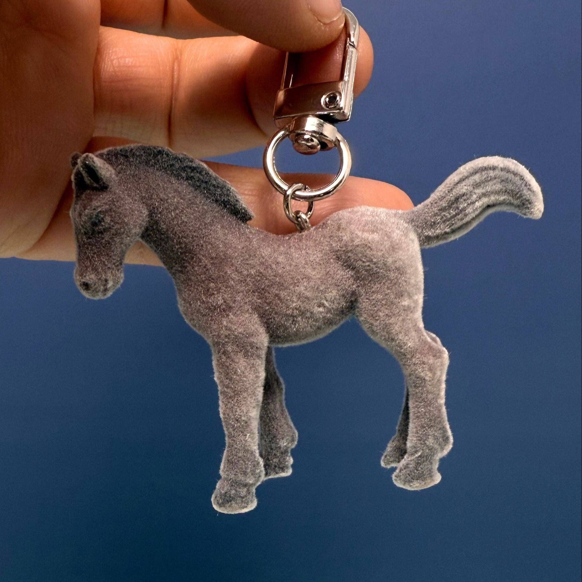 Gray horse-shaped keychain held in a hand against a blue background