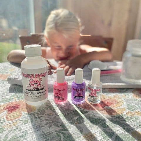 Four bottles of nail polish remover on a table with a child in the background.