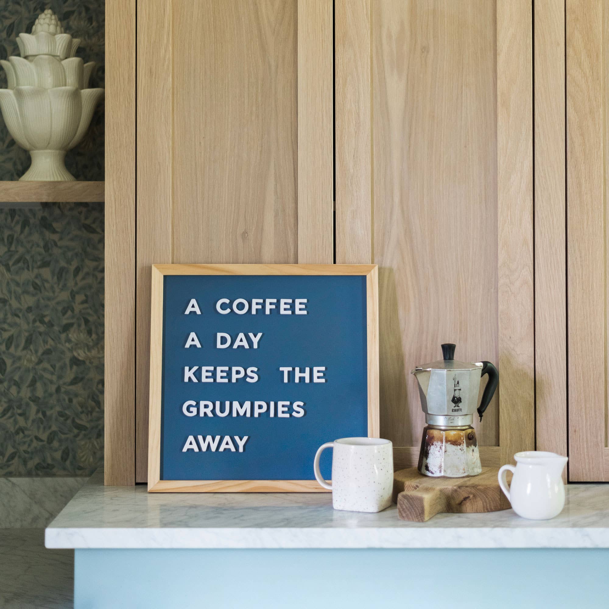 Letter board with coffee-themed quote on a kitchen counter with coffee maker and mugs.