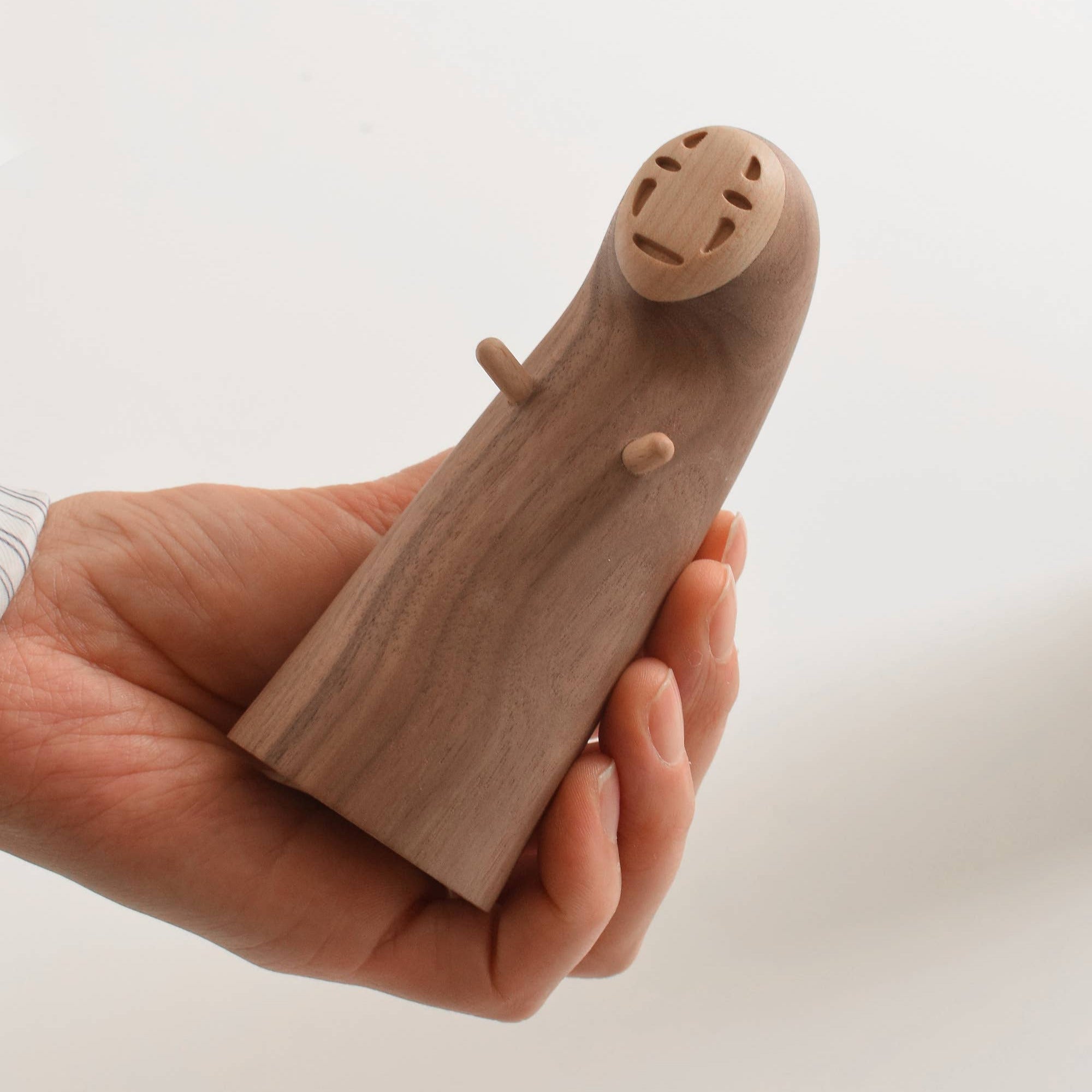Wooden toy shaped like no face held in a hand against a white background
