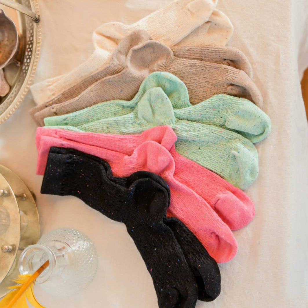 Stack of colorful socks on a textured surface with a book and decorative items.