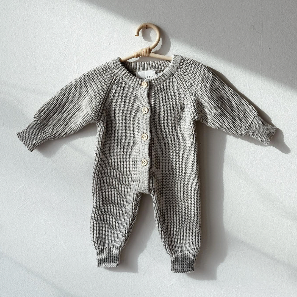 Gray baby romper on a hanger against a light gray background