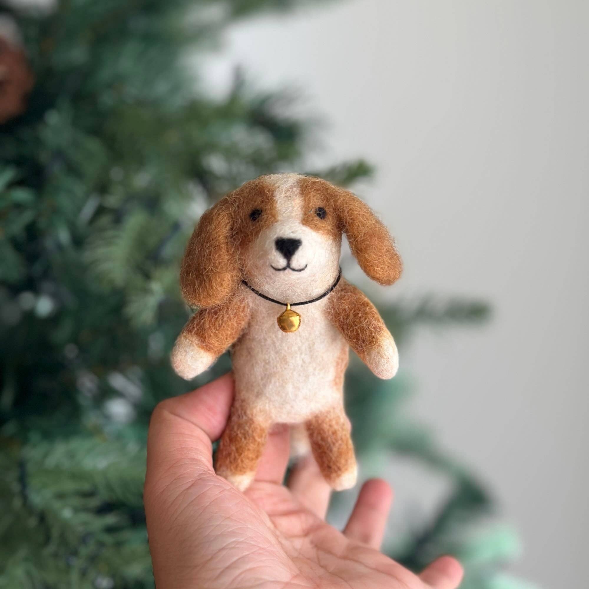 Hand holding a small brown and white dog plush toy with a blurred green background