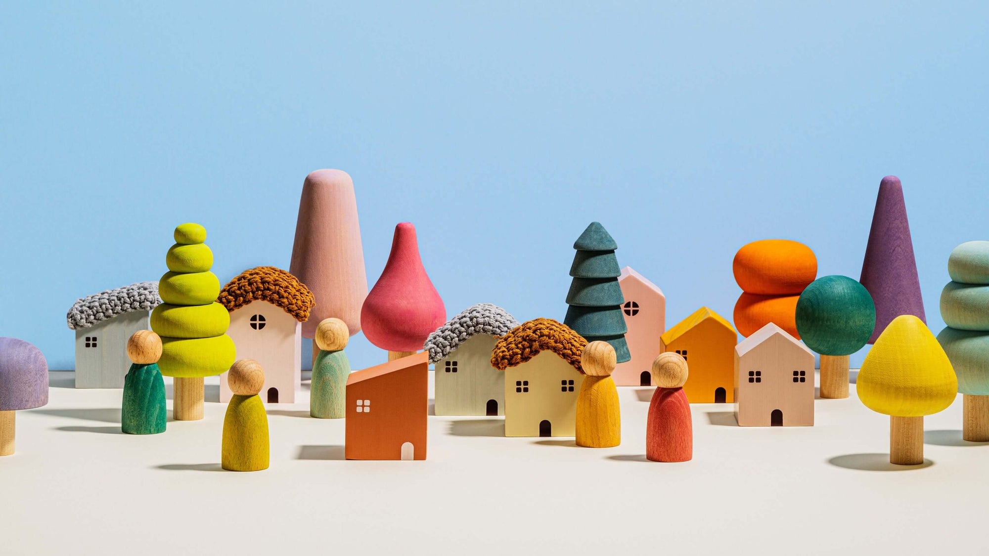 Colorful toy houses and trees on a white surface with a blue sky background
