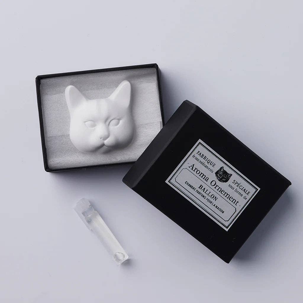 White ceramic cat head sculpture in a black box with 'Aroma Ornement' branding on a light gray background. Diffuser bottle as well.