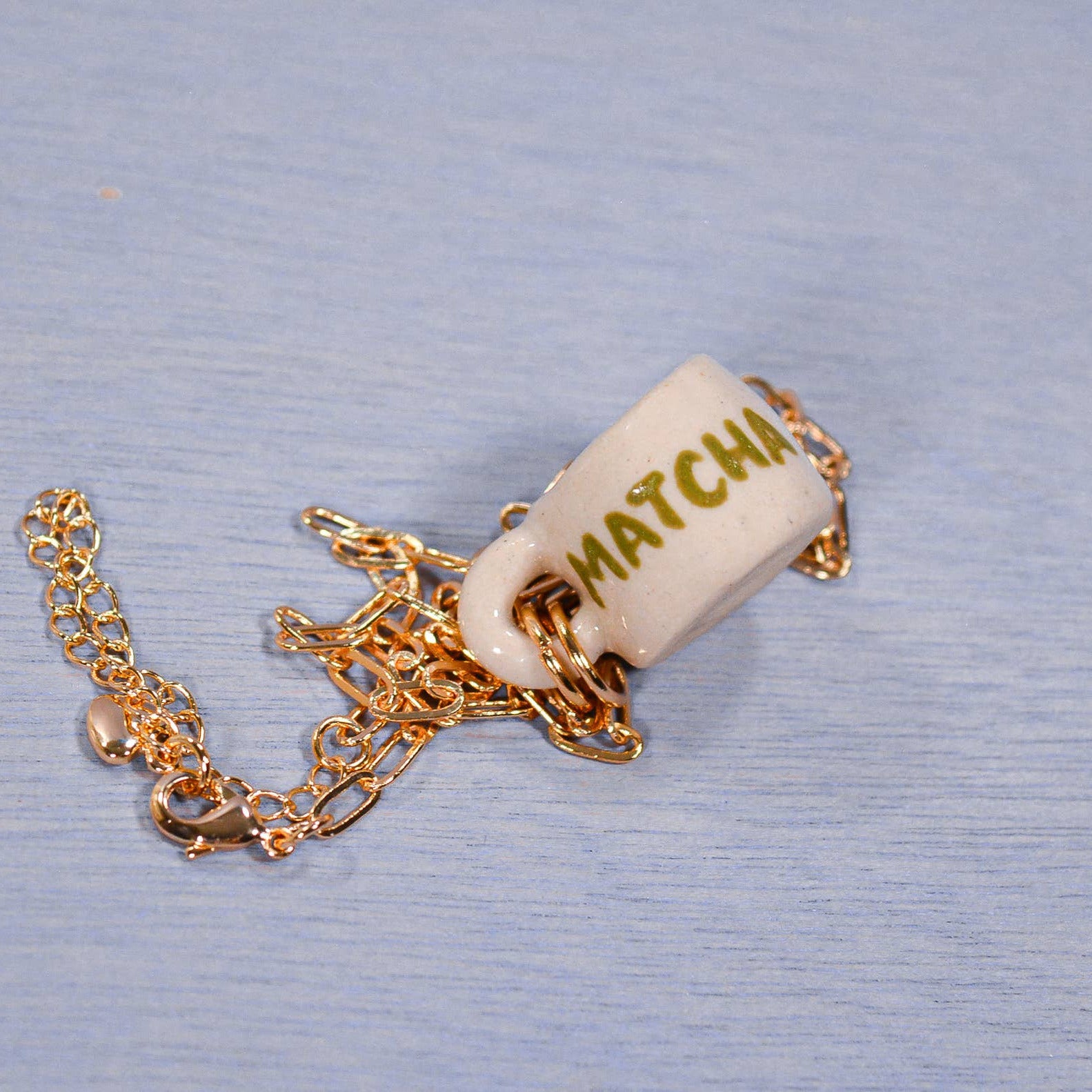 Matchbox charm with gold chain on a blue textured background
