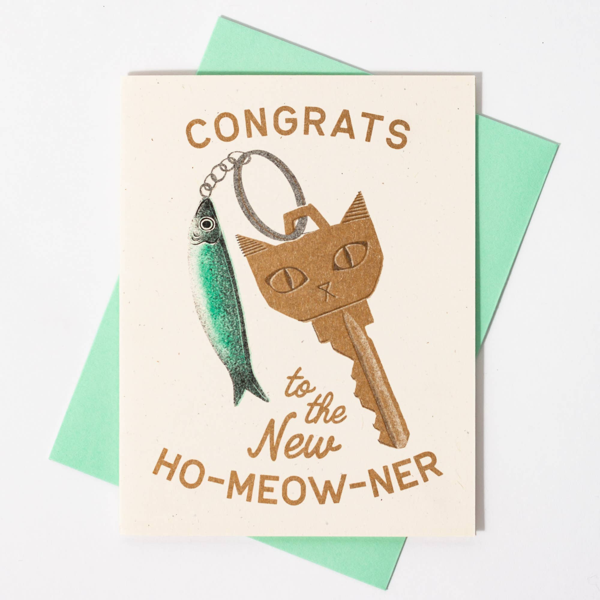 Greeting card with cat key and fish illustration, text 'Congrats to the New Ho-Meow-ner' on a light background.