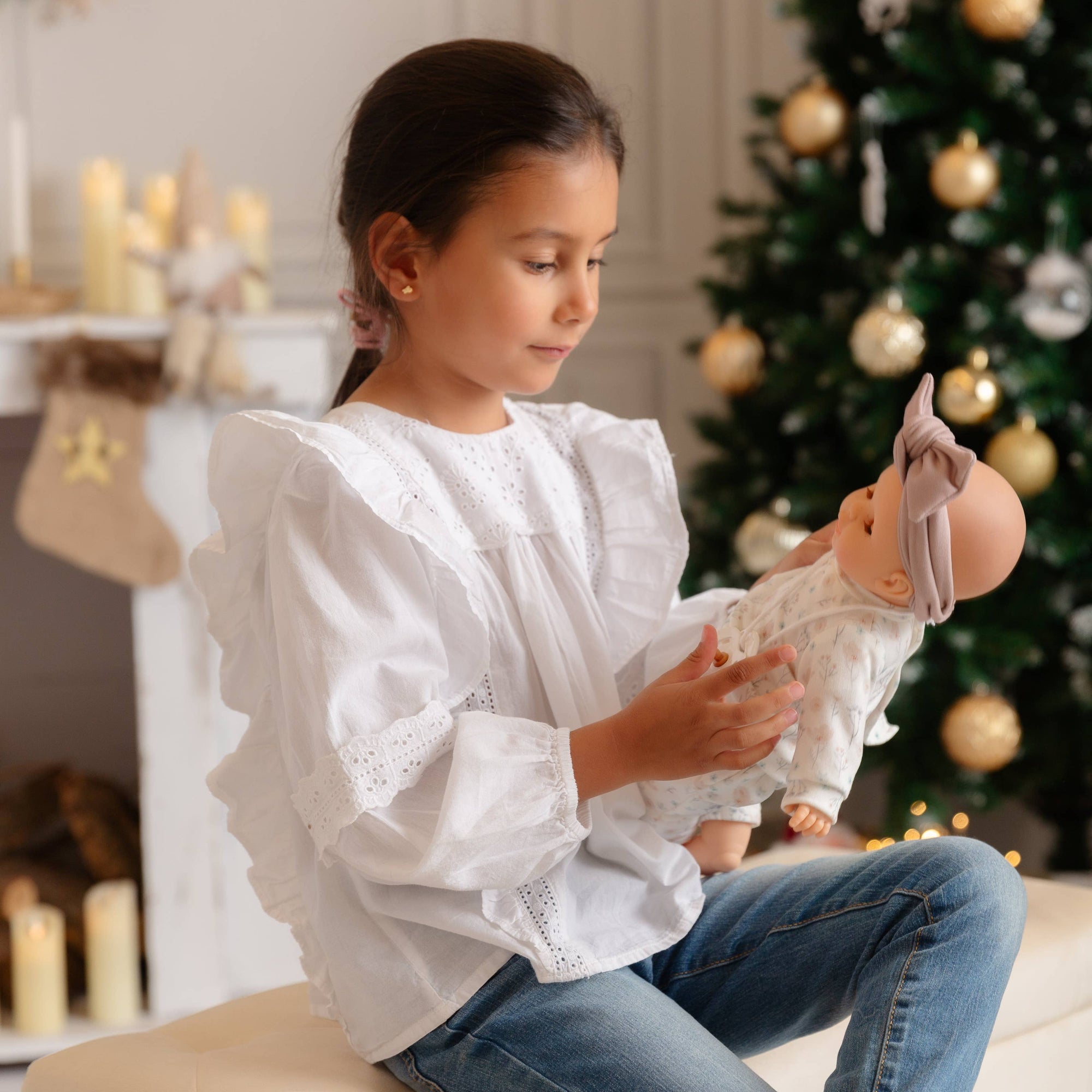 Young girl playing with a doll in a festive room with Christmas tree and decorations.