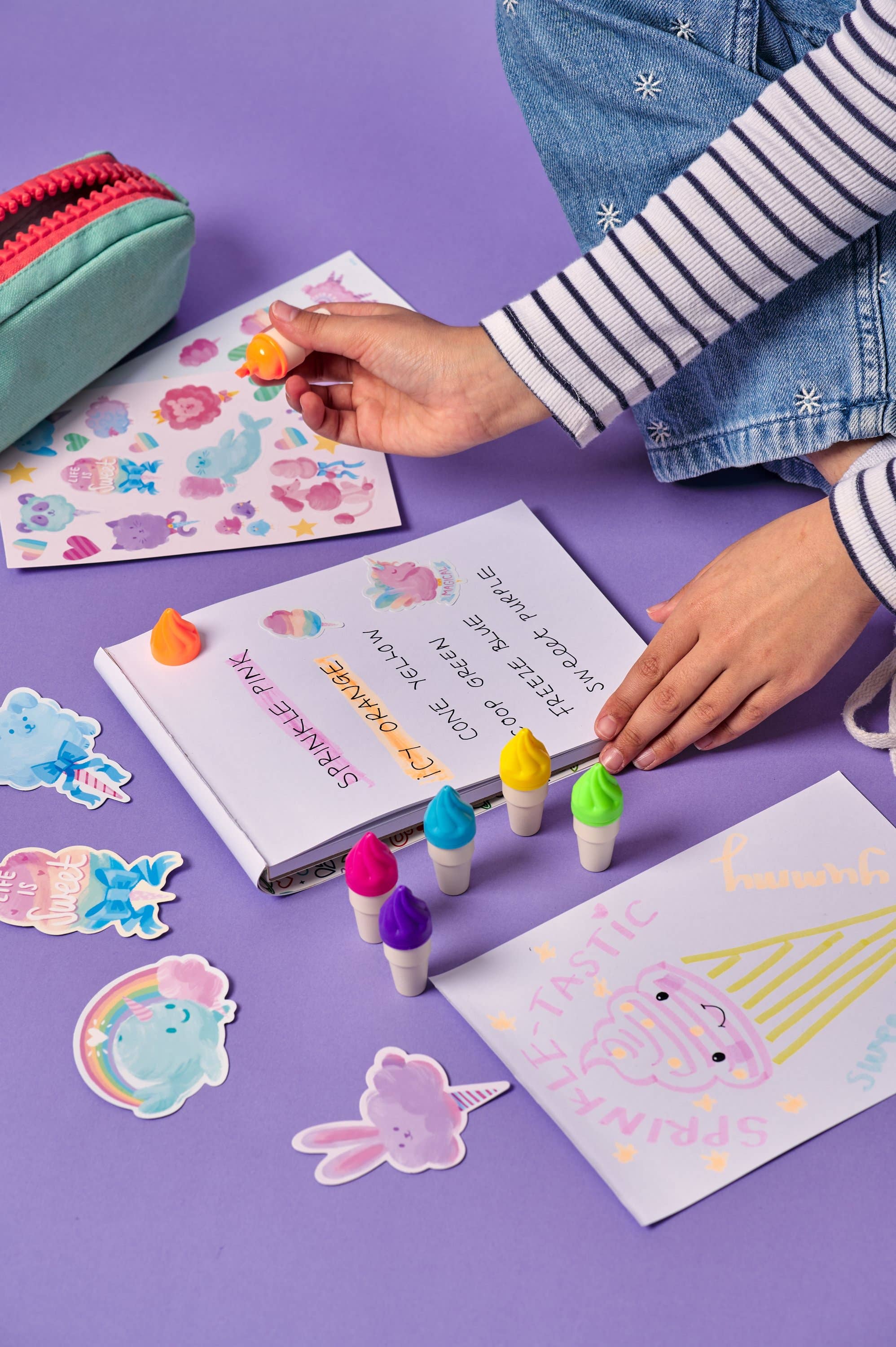 Person decorating a notebook with colorful stickers on a purple surface