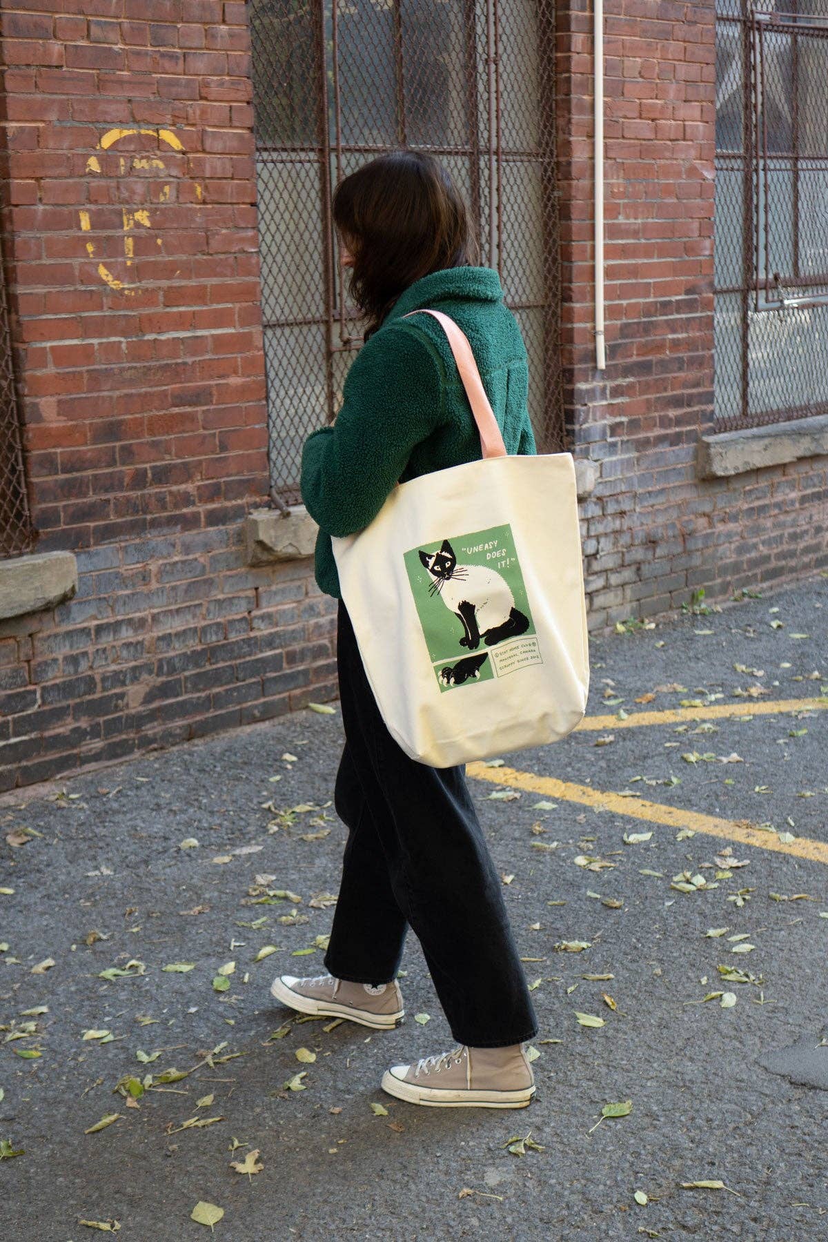 Person walking outdoors holding a white tote bag with a design on it.