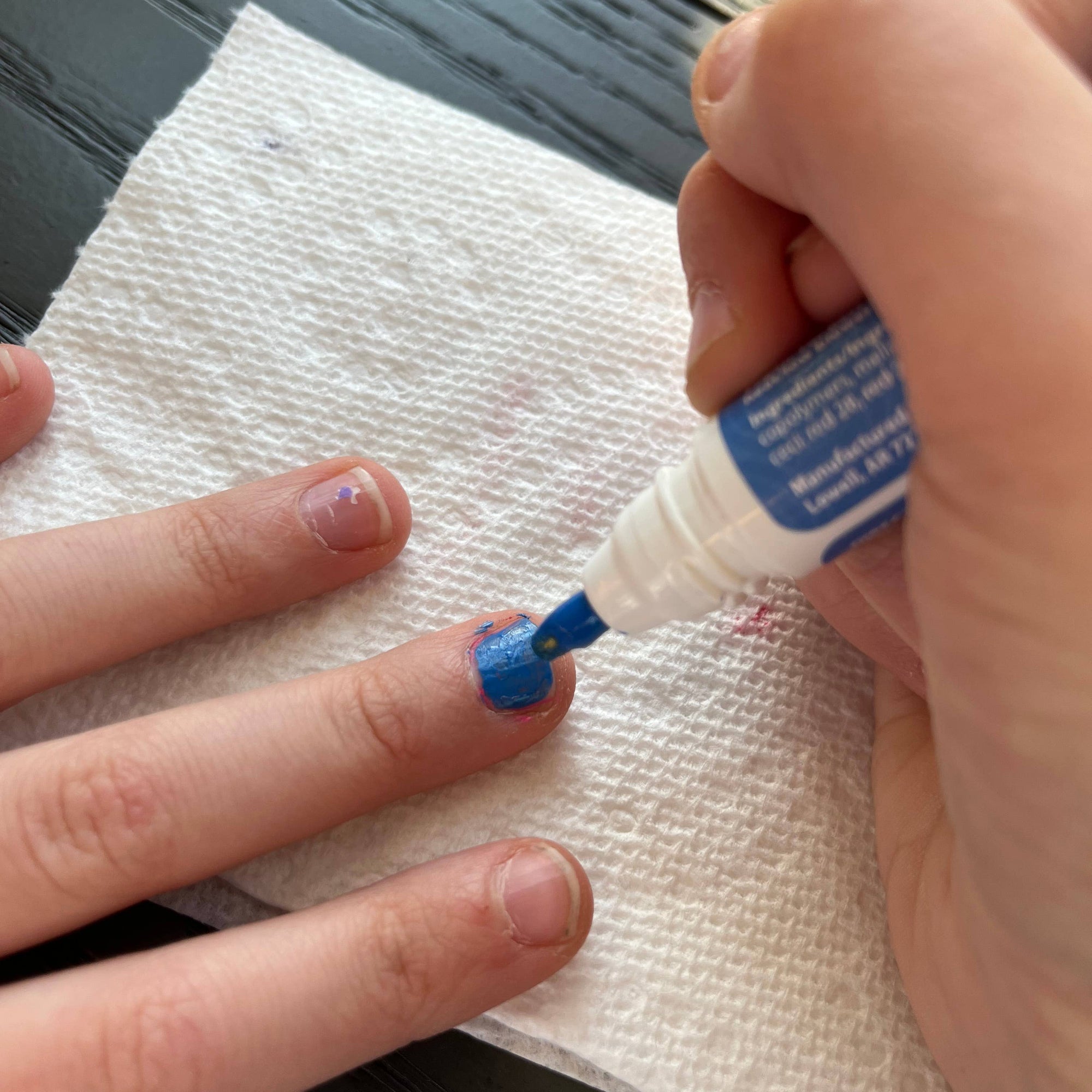 Hand applying a small amount of blue gel to a finger with a white paper towel underneath.