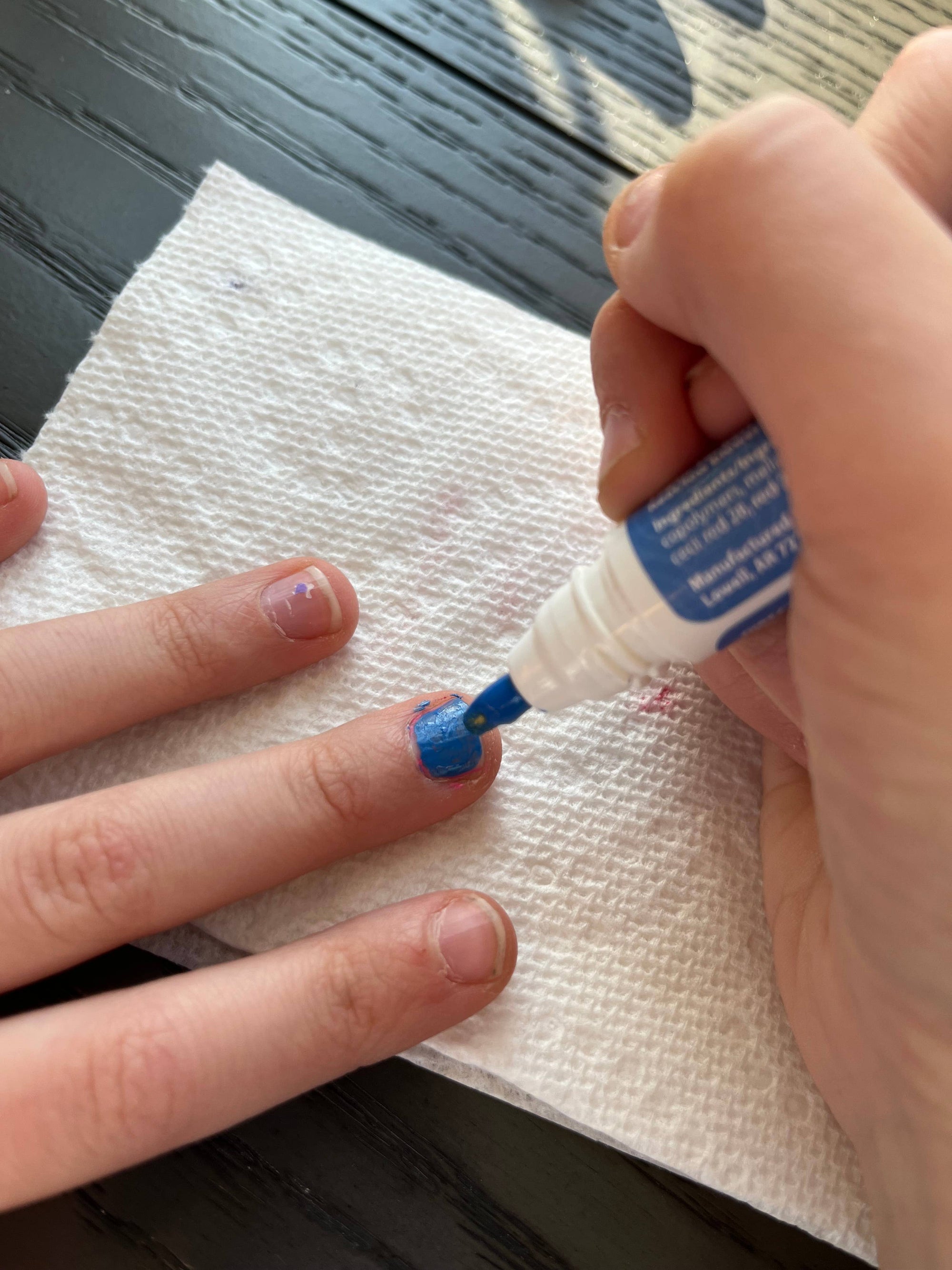 Hand applying a small amount of blue gel to a finger on a white paper towel.