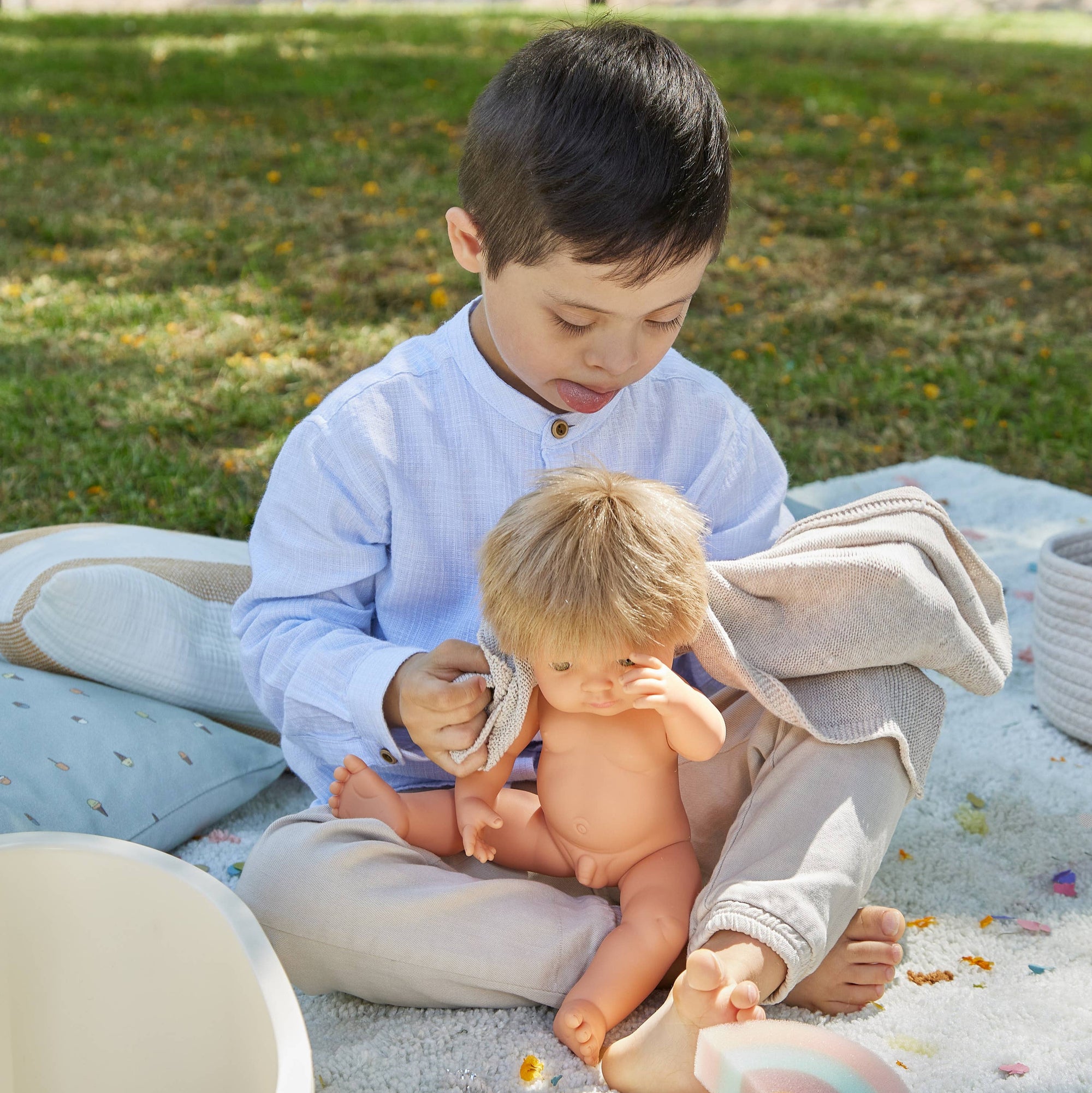 Two children playing with toys on a blanket outdoors.