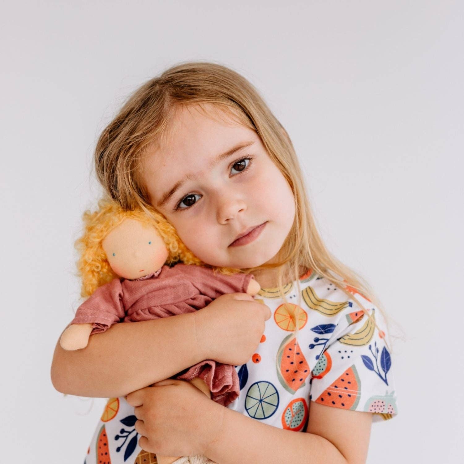 Child holding a doll against a plain background