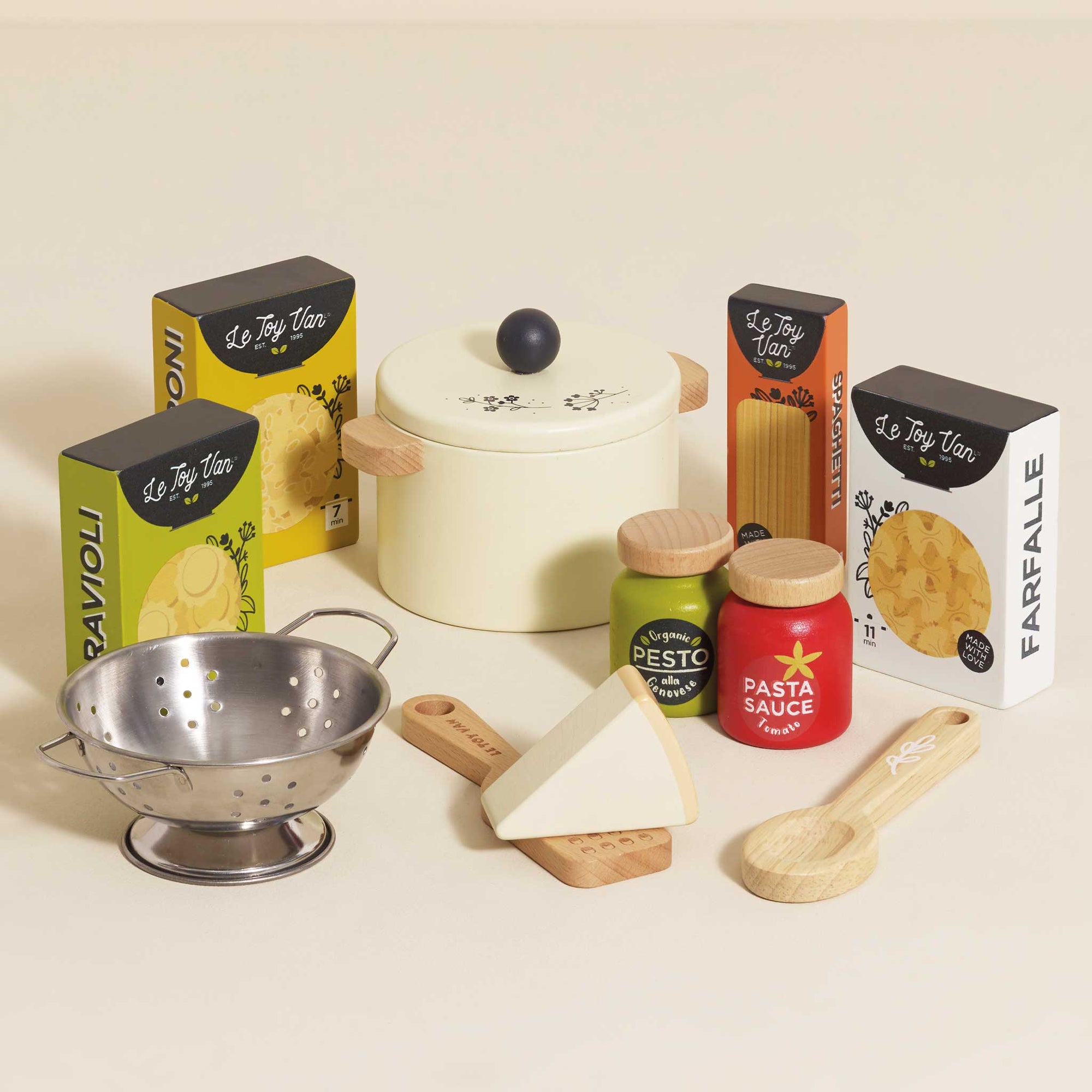 Set of toy kitchen items including a colander, pots, and boxes labeled with pasta brands on a light background.