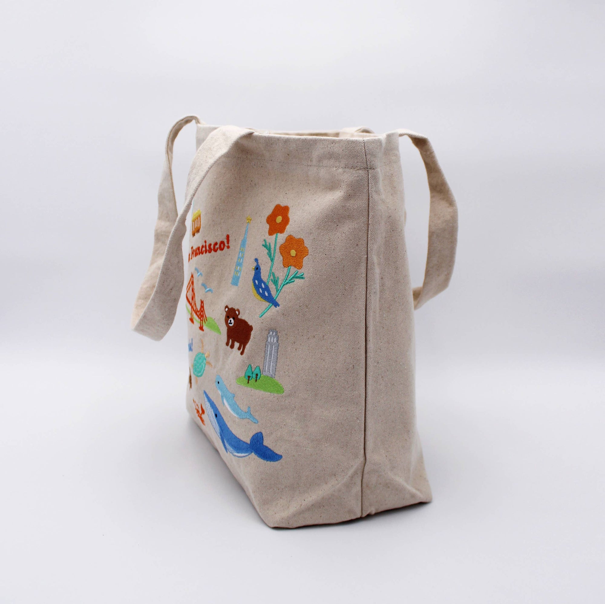 Beige tote bag with colorful animal illustrations on a white background